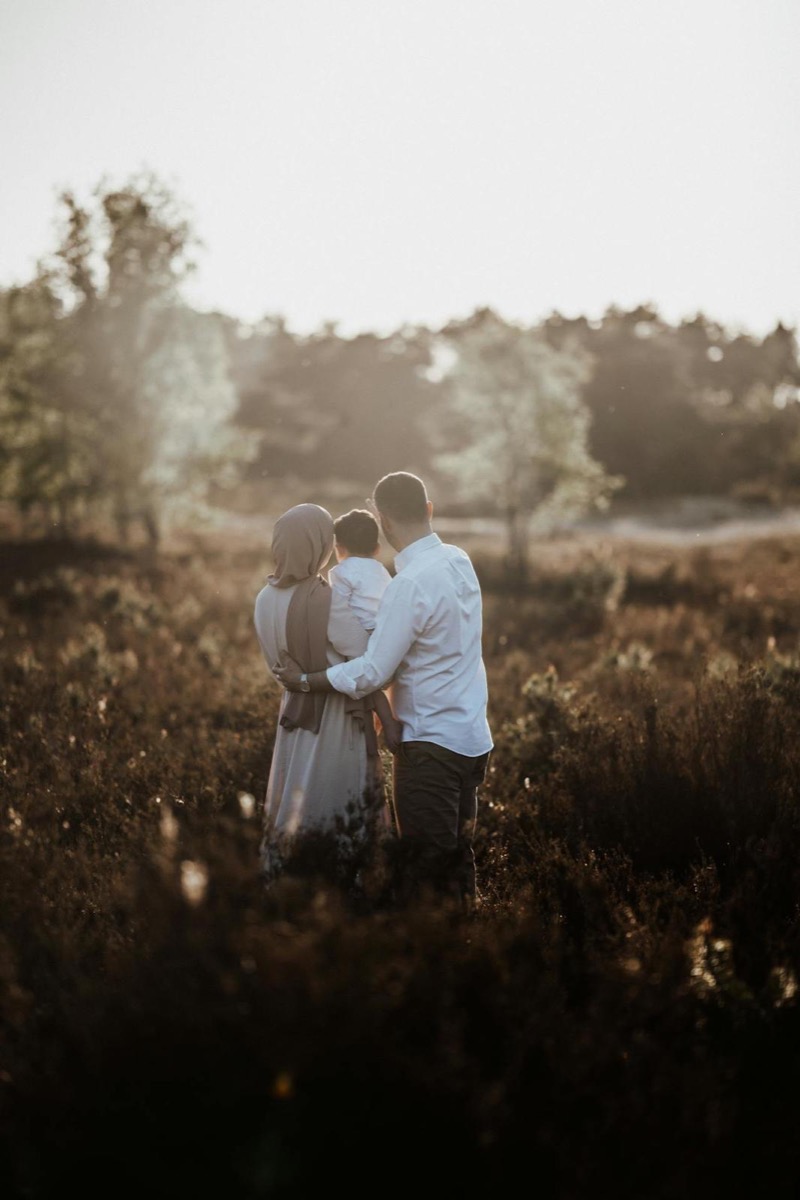 Gezin samen in een veld bij zonsondergang, ouders met hun kind in een hartelijke omhelzing